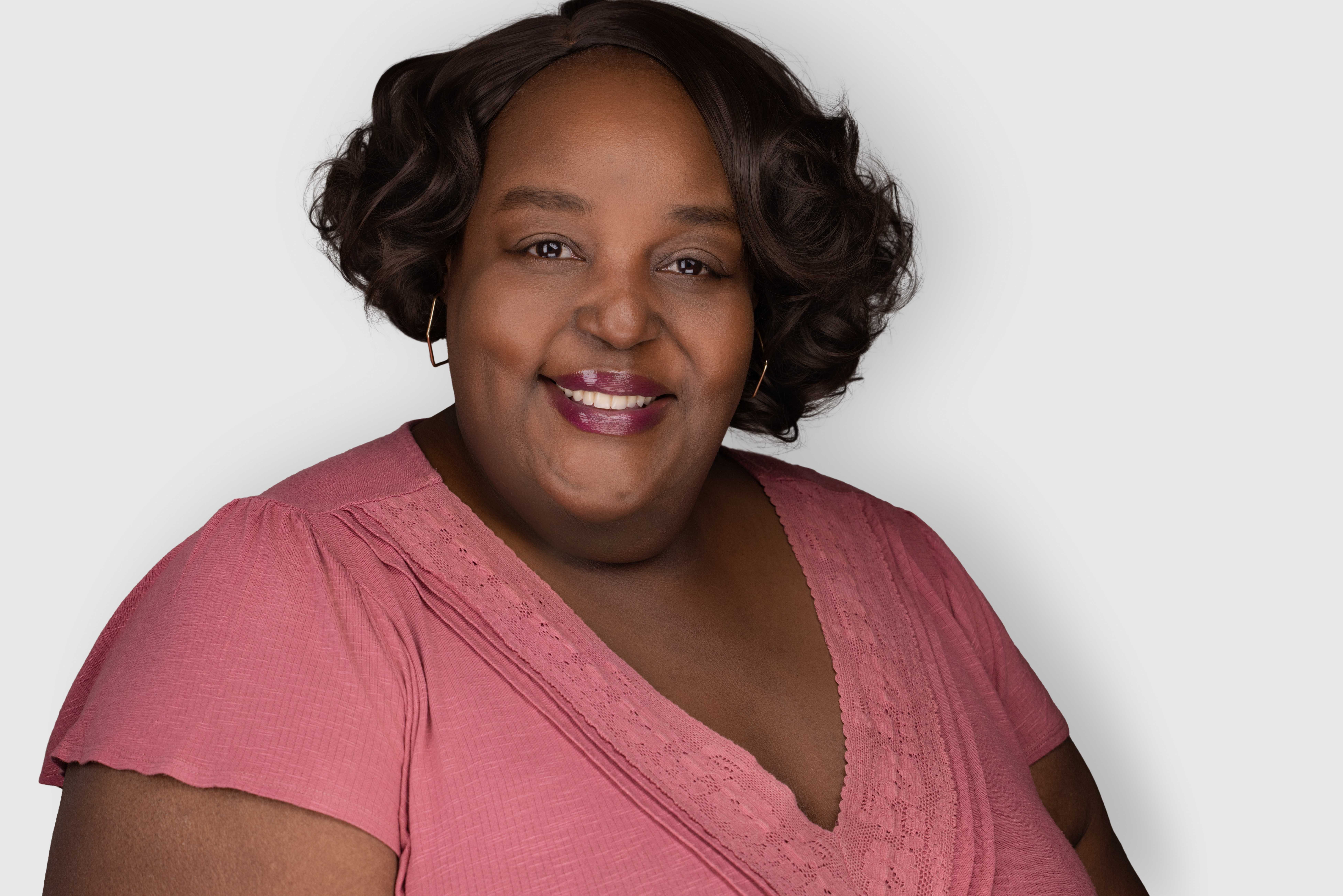 Portrait of Kesha Moore smiling in a pink blouse against a clean light background.