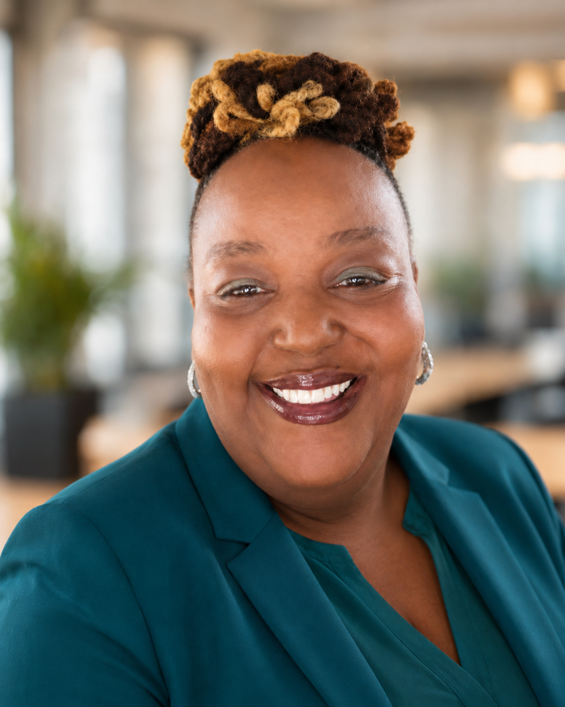 Portrait of Kesha Moore smiling in a teal blazer and coordinating top against a softly blurred office background.